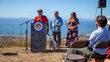 Guest speakers, one of which speaks at podium while holding leashed dog