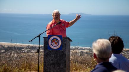 Guest speaker at podium, reaching out one arm backward while speaking