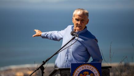 Asm. Bennett at podium, reaching out one arm backward while speaking