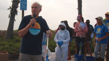 Asm. Bennett holding microphone, speaking to volunteers
