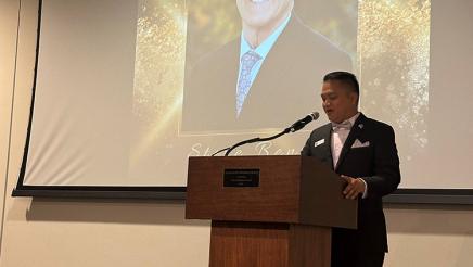 Speaker at podium with large photo of Asm. Bennett on screen in background