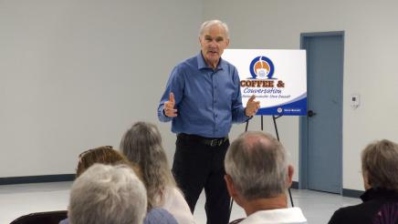 Asm. Bennett standing with large poster in background, speaking to attendees