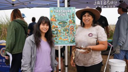 Marianne Parra (left) and daughter Robyn (right) pose in front of 2025 Coastal Cleanup Day poster. 
